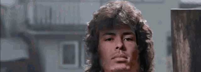 a man with curly hair is standing in front of a building and looking at the camera .