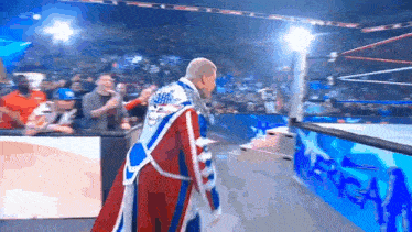 a wrestler in a red , white and blue robe is walking into the ring .