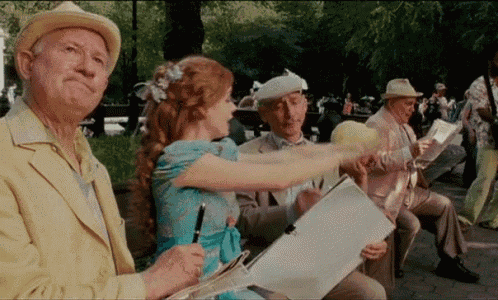 a group of people are sitting on a bench in a park and one of them is holding a piece of paper