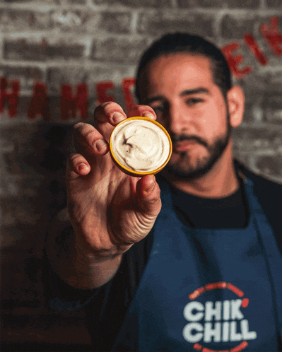 a man wearing an apron that says chik chill holds up a slice of food