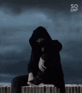 a man in a hooded jacket is sitting on a ledge .