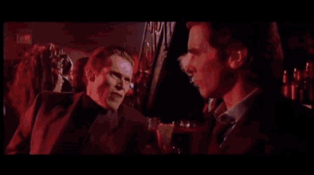 two men in suits and ties are talking in a dark room
