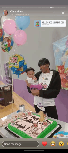 a woman holding a baby next to a birthday cake