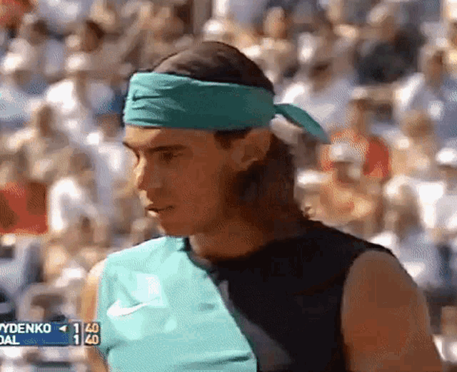 a man wearing a green headband and a black tank top is standing in front of a crowd .