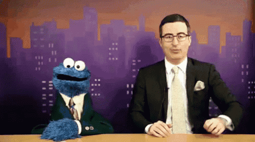 a man in a suit stands next to a cookie monster puppet