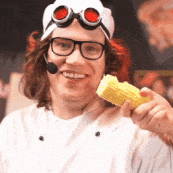 a man wearing a hat and goggles is holding a corn on the cob