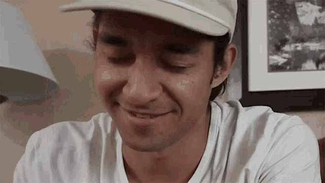 a man wearing a hat and a white shirt smiles