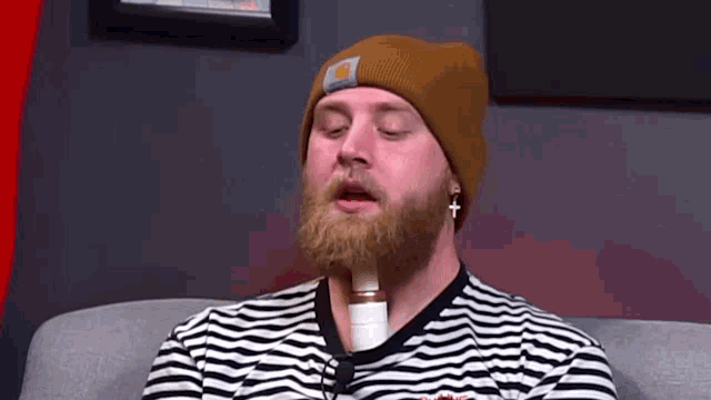 a man with a beard wearing a beanie is sitting on a couch with his eyes closed
