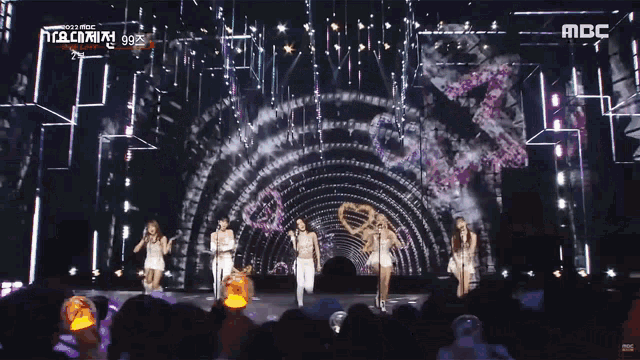 two women singing into microphones in front of a tunnel that says mbc on the bottom