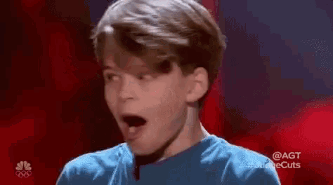 a young boy is covering his mouth with his hands on a red stage .