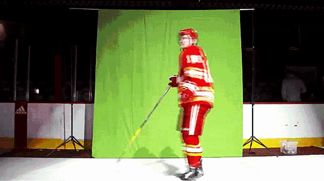 a hockey player is standing in front of a green screen holding a hockey stick