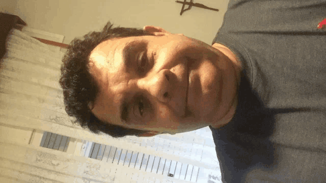 a man wearing a blue shirt is smiling in front of a cross on the wall