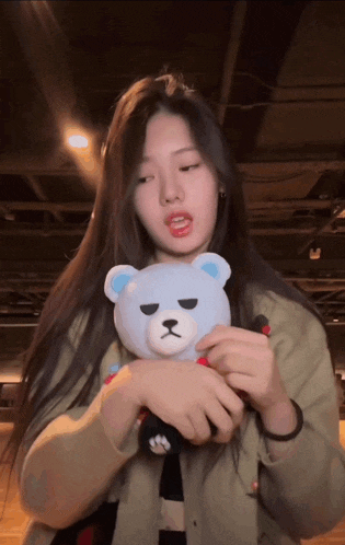a girl is holding a stuffed teddy bear with a black nose and black eyes