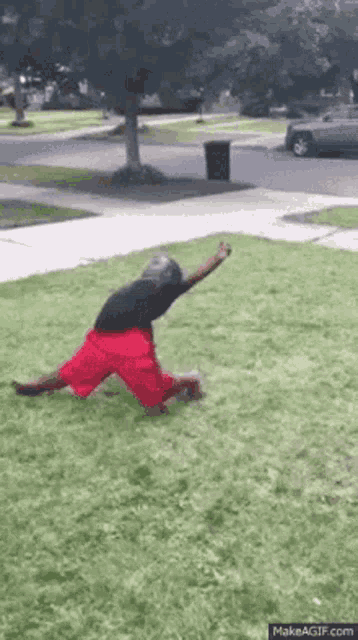 a man is kneeling on the grass in front of a sidewalk .