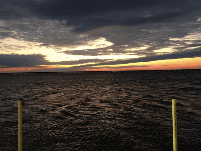sunset over a body of water with a bridge in the distance