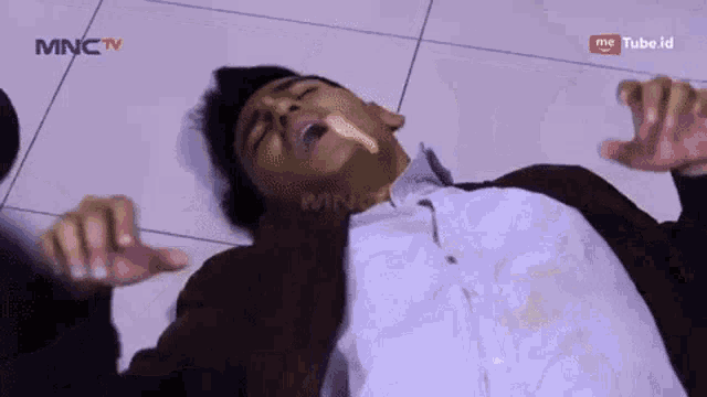 a man is laying on the floor with his mouth open and mnc tv behind him