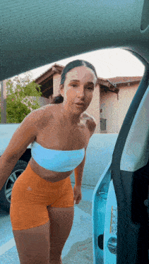 a woman in a white top and orange shorts is standing in front of a blue car