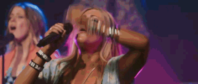 a woman singing into a microphone while wearing a wristband that says life is beautiful