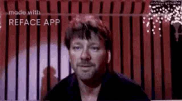 a man with a beard is standing in front of a red curtain and looking at the camera .