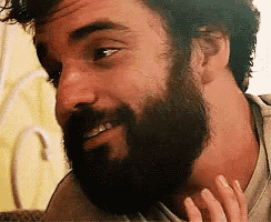 a man with a beard is smiling and looking at the camera while a woman touches his neck .