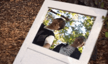 two people are standing in front of a mirror with a reflection of trees