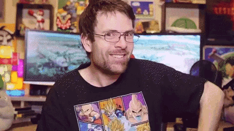 a man wearing glasses and a black shirt with dragon ball characters on it smiles for the camera