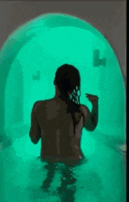 a naked woman is standing in a green bathtub with a green light behind her .