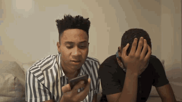 two men are sitting on a couch one is looking at a cell phone