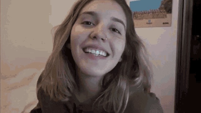 a young woman is smiling and looking at the camera in front of a wall with a picture on it .