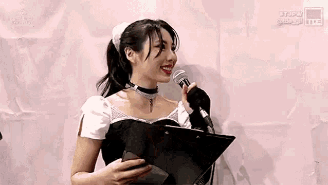 a woman in a maid costume is holding a microphone and a clipboard .