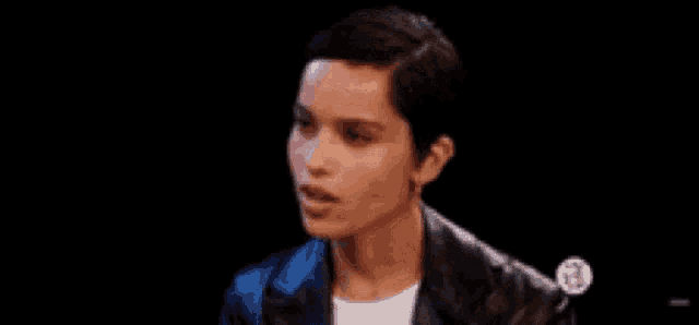a woman with short hair is wearing a leather jacket and earrings and making a funny face .