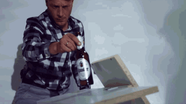 a man in a plaid shirt is opening a bottle of linde