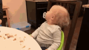 a baby with a pacifier in his mouth sitting at a table