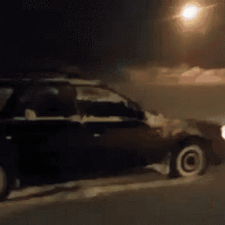 a red car is parked in the snow at night with a street light in the background