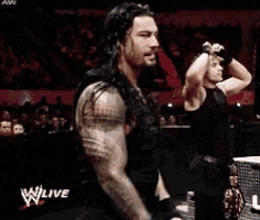a man with a tattoo on his arm is smiling in front of a crowd while a woman stands behind him .