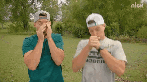 two men covering their faces in a field with nick written on the bottom