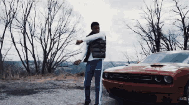 a man is standing in front of a red dodge challenger car