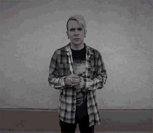a man wearing a plaid shirt stands in front of a white wall