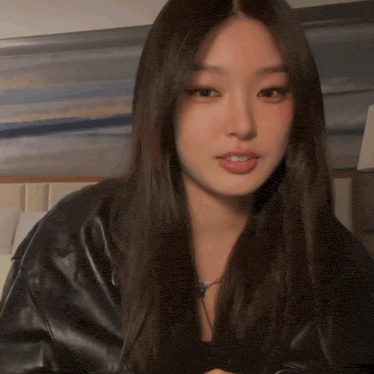 a woman with long dark hair wearing a black leather jacket looks at the camera