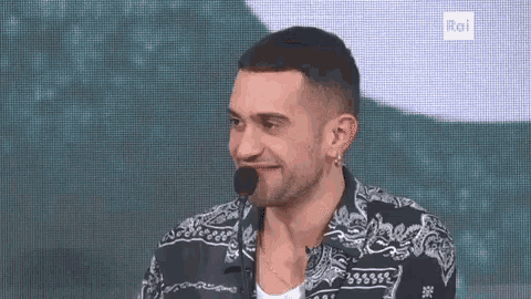a man is talking into a microphone while wearing a paisley shirt and earrings .