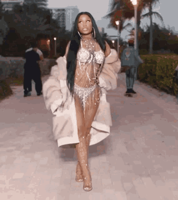 a woman is walking down a sidewalk wearing a fur coat and a bra .