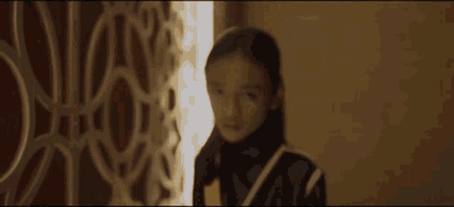 a young girl is standing in front of a wall and looking at the camera