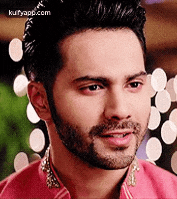 a close up of a man 's face with a beard and a pink shirt .