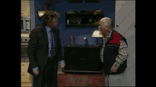 a man in a suit is standing next to another man in a kitchen .