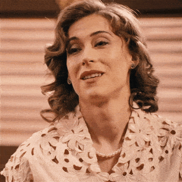 a woman wearing a lace top and pearls smiles