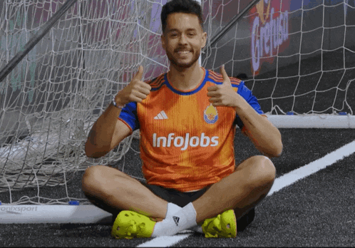 a soccer player wearing an orange and blue jersey that says infojobs is giving a thumbs up