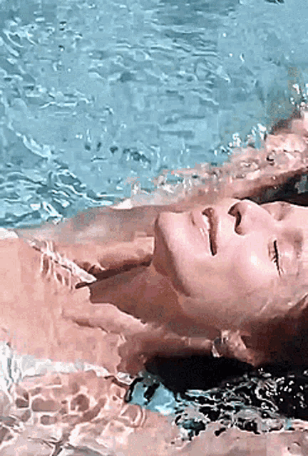 a woman is laying on her back in a pool with her eyes closed