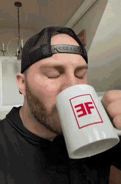 a man with a beard is drinking from a white mug that has the letter ef on it