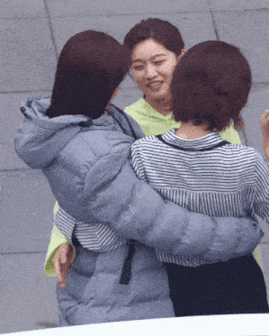 a woman in a striped shirt is hugging another woman in a blue jacket