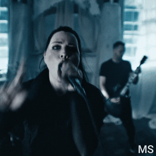 a woman singing into a microphone next to a man playing a guitar with the letters ms on the bottom